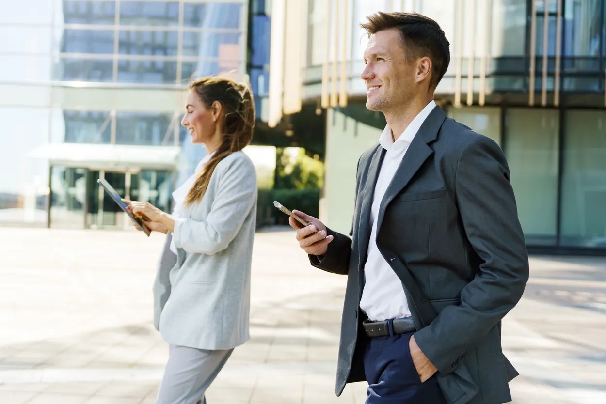 Two business professionals using mobile devices outside an office building